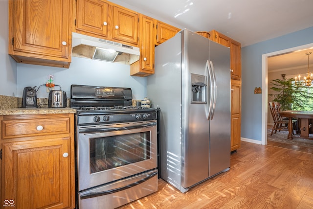 kitchen with crown molding, stainless steel appliances, light stone countertops, light hardwood / wood-style floors, and a chandelier