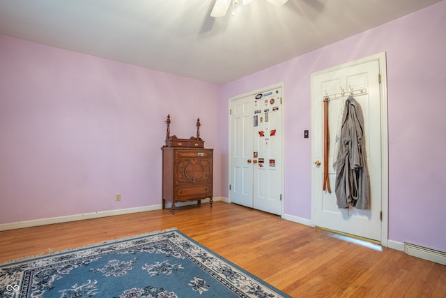 foyer with baseboard heating, hardwood / wood-style flooring, and ceiling fan