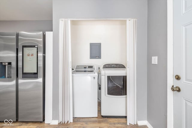 clothes washing area featuring electric panel, light wood-type flooring, and washer and clothes dryer