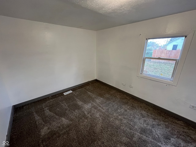 empty room with dark colored carpet and a textured ceiling