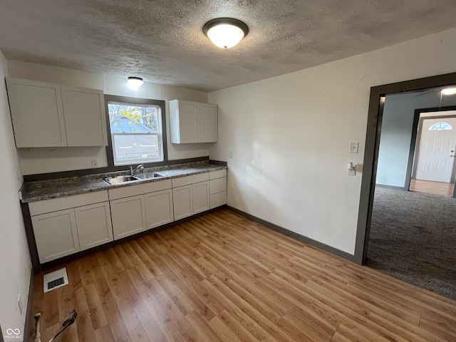 kitchen with white cabinets, light hardwood / wood-style flooring, a textured ceiling, and sink