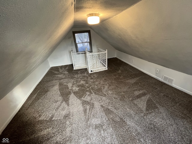 bonus room featuring a textured ceiling, dark colored carpet, and lofted ceiling