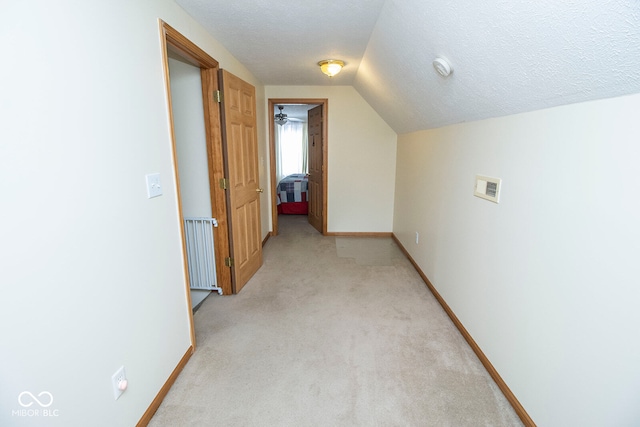 hallway with a textured ceiling, radiator heating unit, light colored carpet, and lofted ceiling