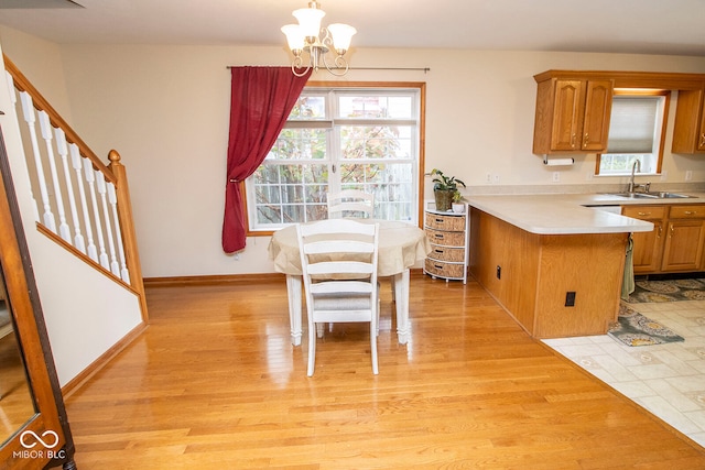 kitchen with an inviting chandelier, sink, hanging light fixtures, light hardwood / wood-style flooring, and kitchen peninsula