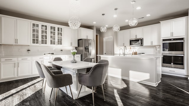 kitchen with white cabinets, stainless steel appliances, hanging light fixtures, and an island with sink