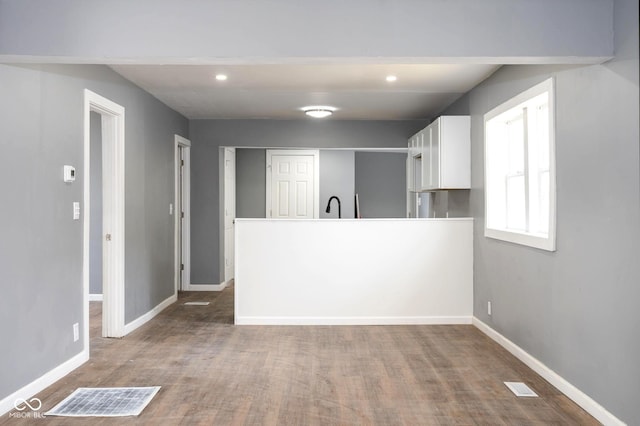 kitchen featuring recessed lighting, white cabinets, wood finished floors, a peninsula, and baseboards