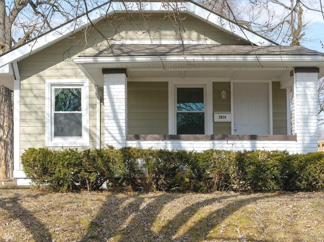 doorway to property featuring covered porch and brick siding