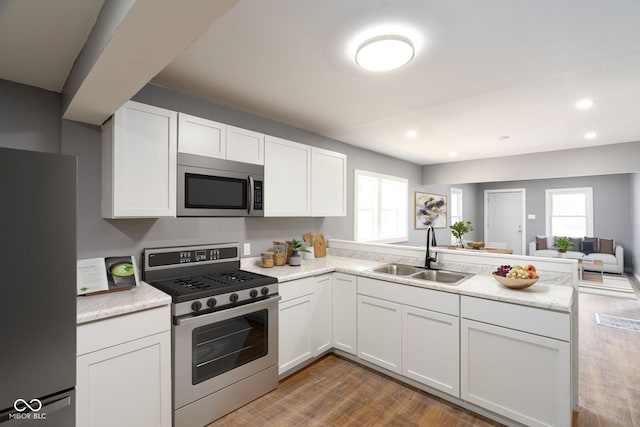 kitchen featuring white cabinets, wood finished floors, a peninsula, stainless steel appliances, and a sink