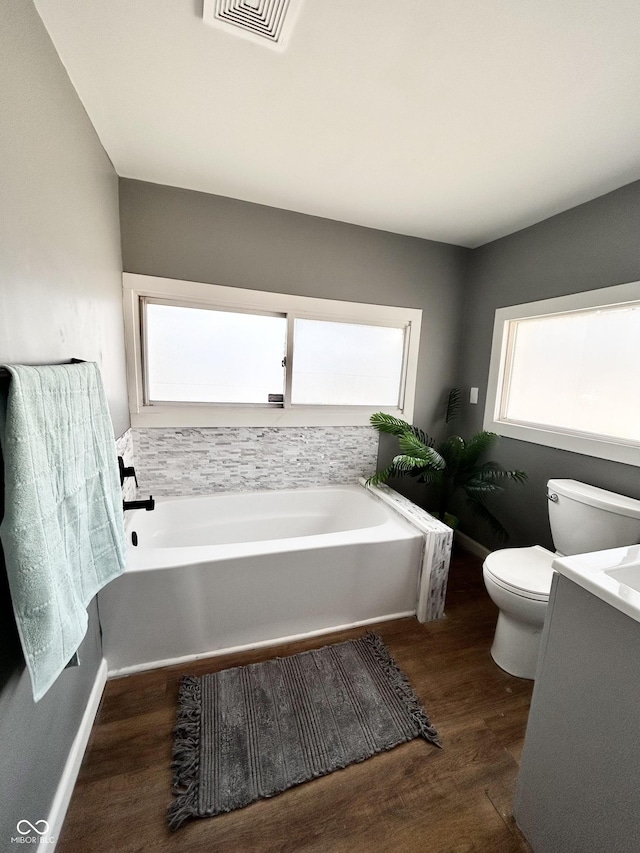 bathroom with visible vents, toilet, vanity, wood finished floors, and a bath