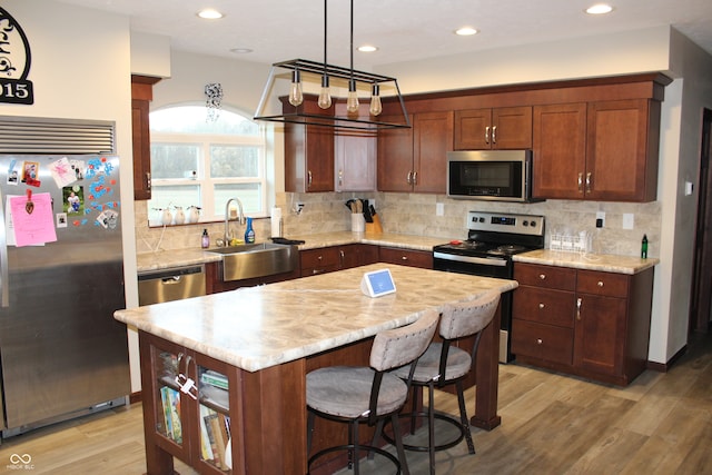 kitchen featuring stainless steel appliances, sink, light wood-type flooring, and a kitchen island