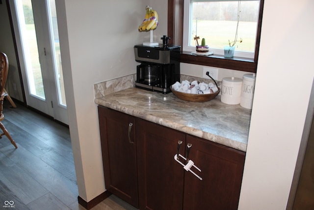 bar with dark brown cabinets, light wood-type flooring, and light stone countertops