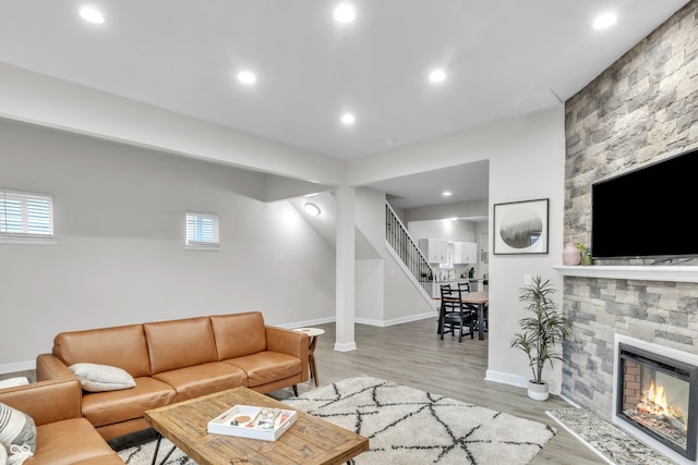 living room featuring a stone fireplace, a healthy amount of sunlight, and light wood-type flooring