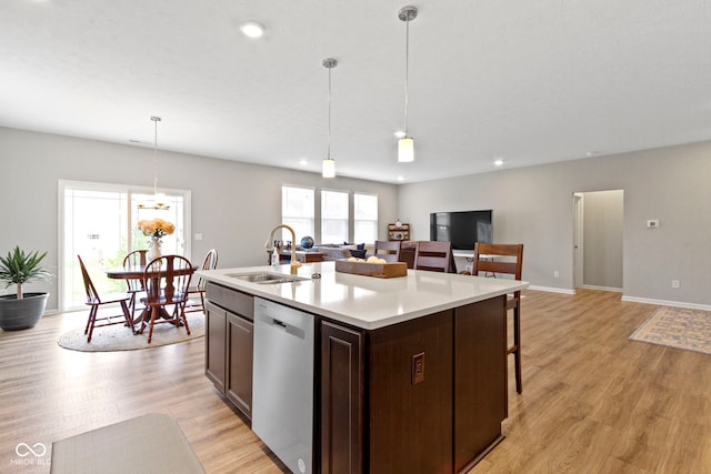 kitchen with light wood-type flooring, stainless steel dishwasher, sink, decorative light fixtures, and an island with sink