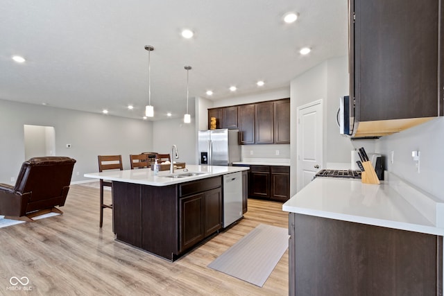 kitchen with sink, pendant lighting, a kitchen island with sink, appliances with stainless steel finishes, and light wood-type flooring