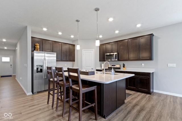 kitchen featuring sink, stainless steel appliances, decorative light fixtures, and light hardwood / wood-style flooring