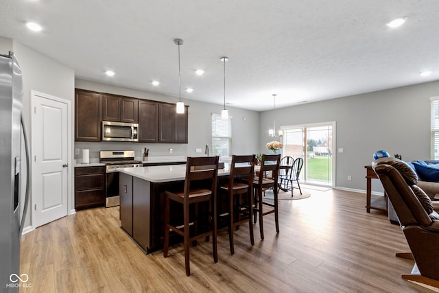 kitchen featuring dark brown cabinetry, a center island, hanging light fixtures, stainless steel appliances, and light hardwood / wood-style flooring