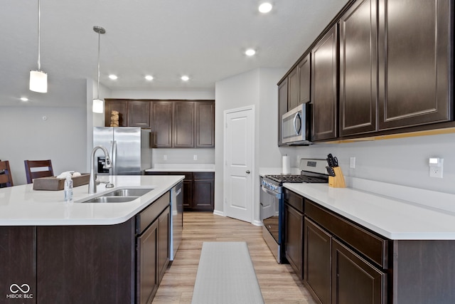 kitchen featuring sink, an island with sink, decorative light fixtures, appliances with stainless steel finishes, and light wood-type flooring