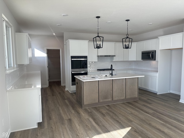 kitchen featuring decorative light fixtures, dark hardwood / wood-style floors, double oven, an island with sink, and white cabinets