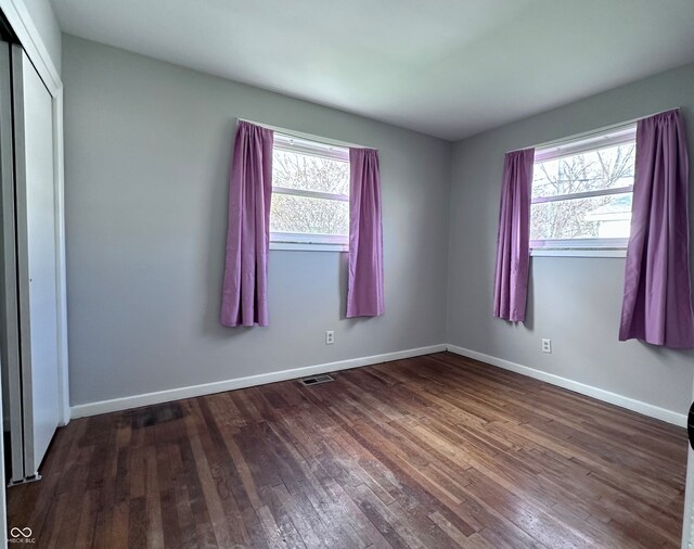 unfurnished bedroom with a closet, dark hardwood / wood-style floors, and multiple windows