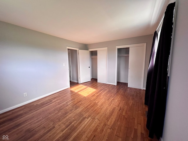 unfurnished bedroom with hardwood / wood-style flooring and multiple closets