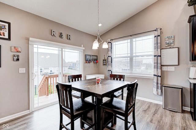 dining area with a chandelier, light wood-type flooring, and vaulted ceiling