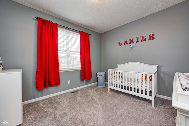 bedroom featuring a crib, a textured ceiling, and carpet floors