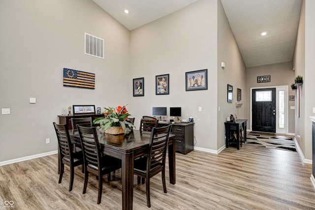 dining area featuring light hardwood / wood-style flooring, high vaulted ceiling, and a textured ceiling