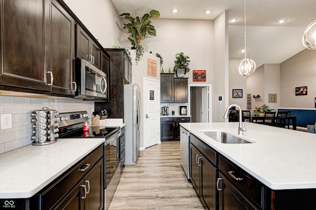 kitchen featuring sink, light hardwood / wood-style floors, decorative light fixtures, a center island with sink, and appliances with stainless steel finishes