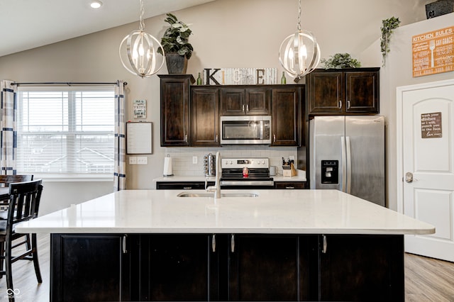 kitchen featuring light stone counters, an island with sink, vaulted ceiling, and appliances with stainless steel finishes