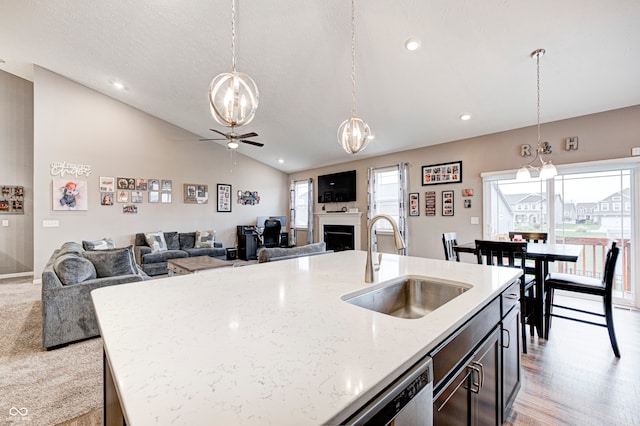 kitchen with sink, light stone counters, an island with sink, decorative light fixtures, and vaulted ceiling