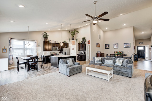 living room with ceiling fan, high vaulted ceiling, light hardwood / wood-style floors, and a textured ceiling