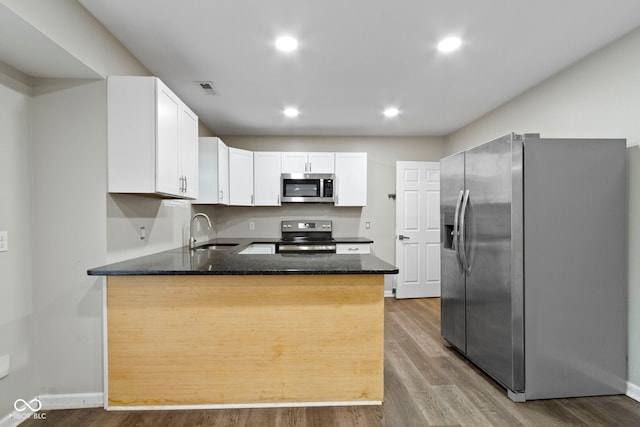 kitchen with kitchen peninsula, stainless steel appliances, sink, wood-type flooring, and white cabinetry