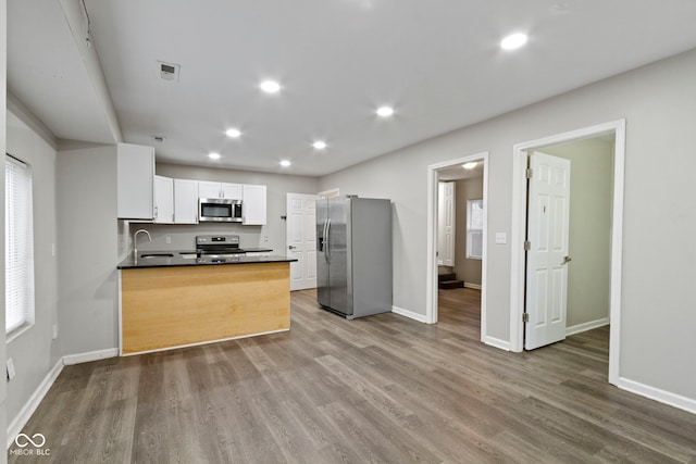 kitchen featuring kitchen peninsula, appliances with stainless steel finishes, sink, white cabinets, and hardwood / wood-style floors