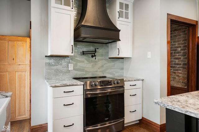 kitchen with light stone counters, white cabinets, stainless steel range with electric stovetop, backsplash, and premium range hood