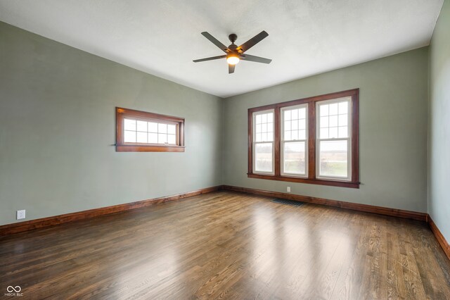 empty room with dark wood-type flooring, a wealth of natural light, and ceiling fan
