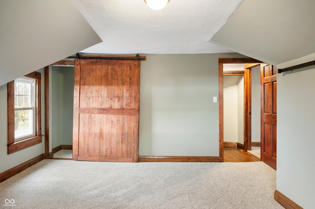 unfurnished bedroom featuring a textured ceiling, light colored carpet, and a barn door