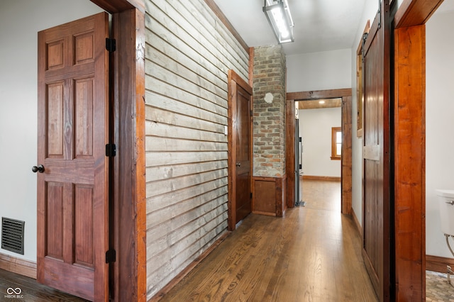 hall with wood-type flooring, a barn door, and brick wall