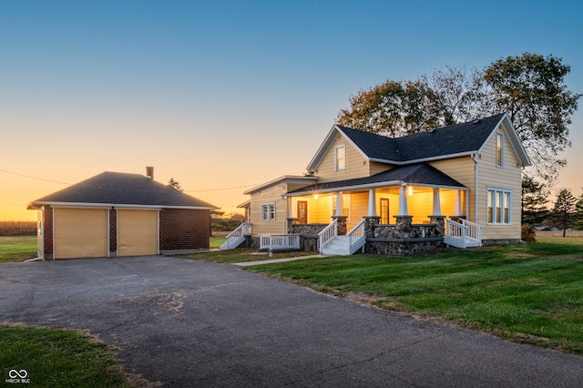 view of front facade featuring an outbuilding, a garage, covered porch, and a lawn