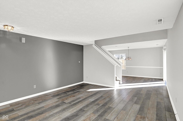 unfurnished room with a notable chandelier, dark hardwood / wood-style flooring, and a textured ceiling