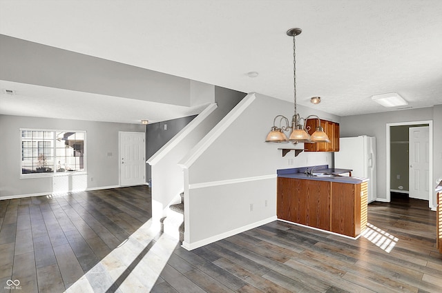 kitchen with kitchen peninsula, hanging light fixtures, dark wood-type flooring, and sink