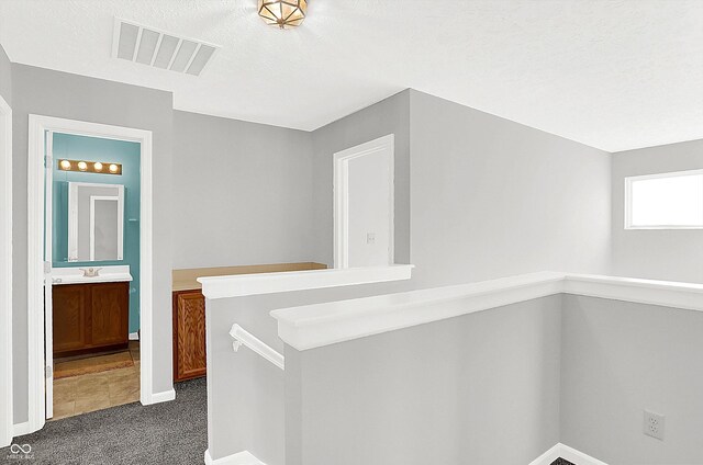 hallway with dark colored carpet, a textured ceiling, and sink