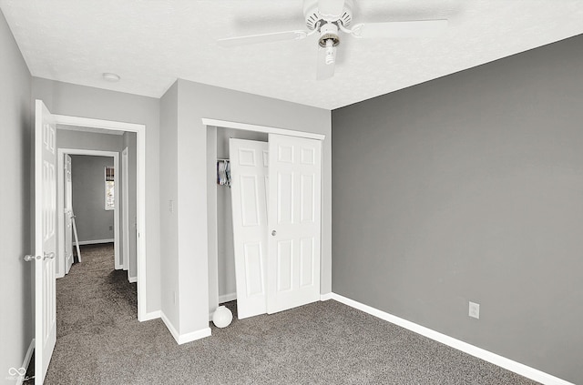 unfurnished bedroom with ceiling fan, dark carpet, a textured ceiling, and a closet