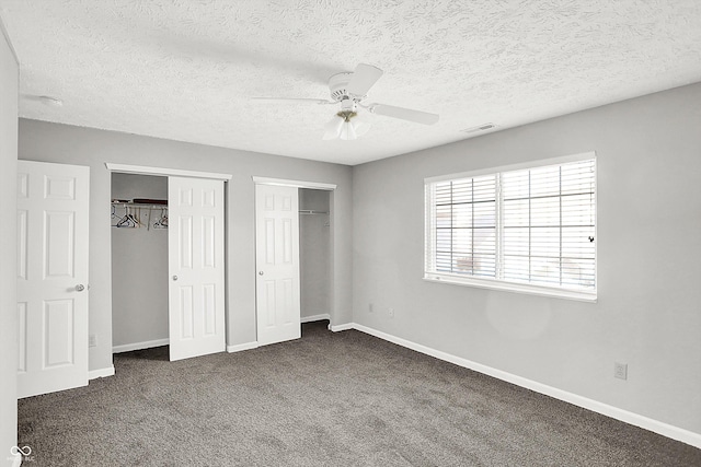 unfurnished bedroom with dark colored carpet, ceiling fan, a textured ceiling, and multiple closets