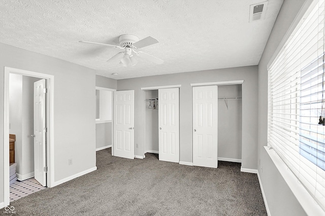 unfurnished bedroom featuring dark carpet, two closets, ensuite bathroom, ceiling fan, and a textured ceiling