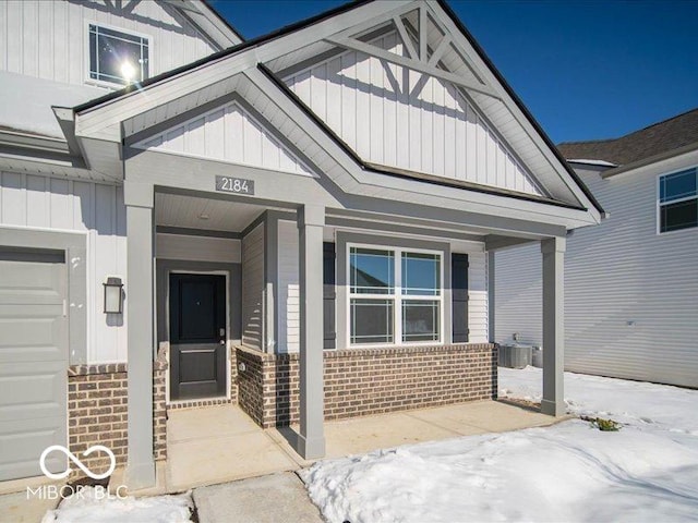 snow covered property entrance featuring cooling unit, a garage, and covered porch