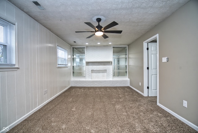 unfurnished living room featuring wood walls, carpet flooring, ceiling fan, a fireplace, and a textured ceiling