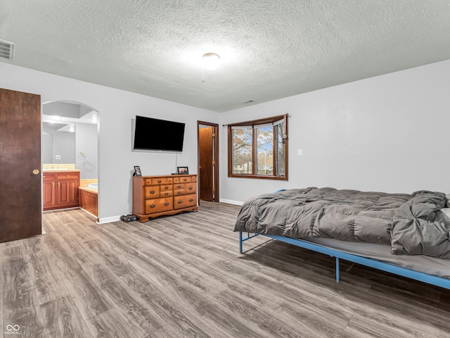 bedroom featuring a textured ceiling, light hardwood / wood-style flooring, and ensuite bath