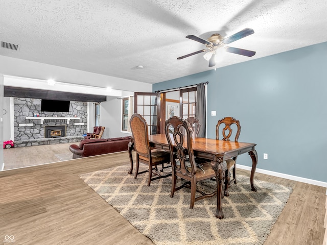 dining area with hardwood / wood-style floors, ceiling fan, a stone fireplace, and a textured ceiling