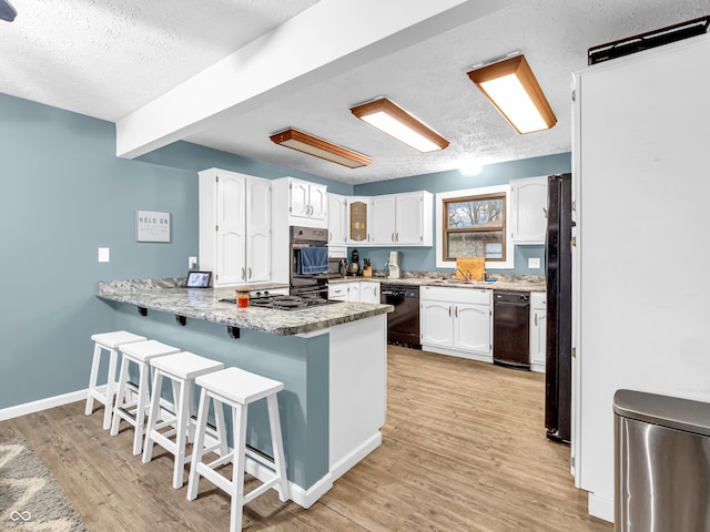 kitchen featuring kitchen peninsula, light hardwood / wood-style floors, a textured ceiling, white cabinets, and black appliances