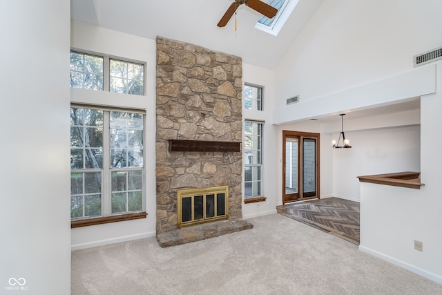 unfurnished living room featuring high vaulted ceiling, a skylight, a stone fireplace, and carpet floors